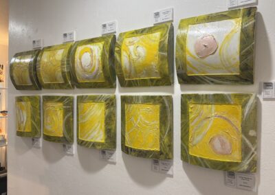 Satellites of Energy, 2025, 10 pieces at 10x10" each, Acrylic on wooden convex frame. Price: $400 for all 10 pieces. Artist's description: A series of 10 square paintings. Luminous gold, yellow, and white. With thick, layered texture. Circular motion and light building in each panel. Can be exhibited as a set or individually. Satellites are pieces of the larger work Energy. Each of the ten panels holds its own motion - a swirl, a pulse, a gathering - but together they create collective power. Like people in a community, each satellite is complete on its own and stronger in orbit with others. The warm, harvest tones speak to nourishment, sunlight, and care. This series honors the small acts and individual voices that when joined, shift things, "do something." Satellites remind us that change is built piece by piece, person by person.
